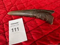 Buffalo horn sculpture with carved human face on a red quilted fabric background, Maxsold lot tag 111 visible