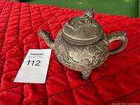 Side view of vintage metal teapot showing embossed patterns, ornate lid, handle, and spout