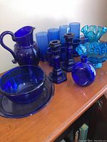 Overall view of blue glassware featuring pitcher, tall glasses, blue candle sticks, bowl, plate, candy dish, and small figurines.