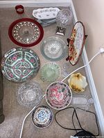 Full overview of assorted bowls, plates, serving dishes, cake pedestal, candle globe and glassware on floor