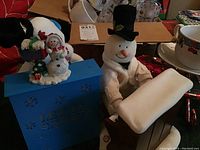 Photo of two musical snowmen figurines; one on blue base with 'Let It Snow,' the other holding a scroll