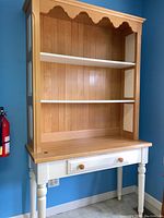 Front view of wood desk with attached hutch showing shelves and single drawer.