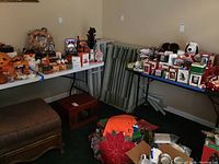 Three folding tables displayed indoors surrounded by holiday decorations and other items. Tables show foldable design and metal leg frames.
