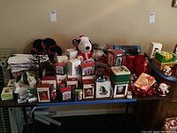 Full table view showing various Hallmark Keepsake ornaments in boxes, Snoopy plush, assorted Christmas decorations and towels.