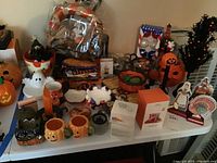 Photo of Halloween and Thanksgiving decorations including pumpkin and ghost figurines, mugs, festive baskets, and framed items on a table