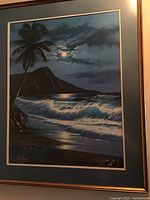 Framed print featuring moonlight over ocean waves, a palm tree, and a mountain under a cloudy sky.