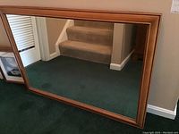 Full view of rectangular framed wall mirror on floor with staircase background, showing the wooden frame and reflective glass