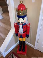 Full view of the tall red and gold wooden nutcracker figure by a staircase