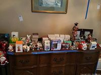 Wide view of the ornaments, snow globes, and boxed items arranged on wooden dresser, includes holiday figurines and collectibles