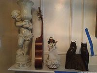 Photo showing the 22 inch cherub planter, the ukulele missing strings, the musical doll in white dress, and the wooden owl figurine setup together.