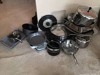 Image showing a large collection of metal pots and pans, including stack of pots with lids, large baking sheet, various round pans, and some black handled cookware.
