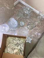 Overview of the assembled glass items including punch bowl, pitchers, bowls, and dishes placed on carpeted floor near corner wall.