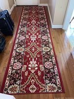 Full view of the carpet runner laid on hardwood floor showing the overall red floral and geometric pattern with a dark border and finished edges.