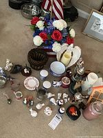 Overall lot showing various household collectibles including shakers, steins, candles, floral arrangement, basket, and small figurines.