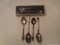 Six sterling silver collectible spoons displayed on flat surface with one boxed spoon showing detailed metalwork on handle.