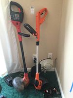 Two cordless string trimmers, one red/black (CST2000) and one orange/black (LST220), standing upright with visible handles and trimming guards
