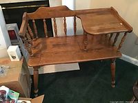 Wooden vintage telephone bench by Ethan Allen with side table surface and spindle backrest, shown from a slight angle indoors with green carpet and surrounding boxes.