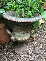 Ornate cast metal urn planter with grass inside, side view