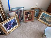 Eight framed art pieces grouped together on floor, showcasing various sizes and elaborate gold and wood frames with classical reproduction artwork.