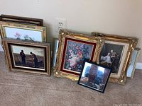 Seven framed art pieces leaned against wall showing varied subjects and frame styles