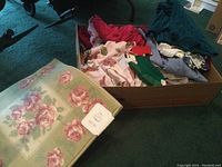 Photo showing Simply Shabby Chic floral 2x3 rug rolled with tag visible alongside a box of women's clothing items including Christmas socks and various garments.