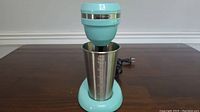 Front view of the Brentwood milkshake maker showing the full unit with the stainless steel cup attached on a dark wooden surface.