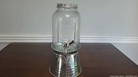 Full view of the clear glass beverage dispenser on metal stand with spigot and lid.