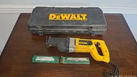 DeWalt reciprocating saw with two sealed Greenlee saw blades and black DeWalt carrying case on wood surface.