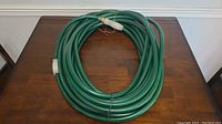 Coiled green garden hose on a wooden table showing the full length and condition.