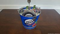 Photo of branded metal bucket with spoons inside, featuring Mott's Clamato Caesar 40th anniversary graphics in blue.