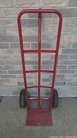 Front view of red metal work dolly showing tubular frame, mesh lower section, and base plate