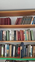Three shelves of assorted books including hardcover novels and nonfiction works with varied spine colors and wear.