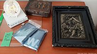 View of brass 40 year calendar plate, carved wooden box, packaged Scotland.com rain ponchos, and wood frame wall art with embossed design.