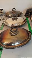 Set of three silverplate covered serving dishes, all oval, footed with ornate bead pattern edges, lids with loop handles, and side handles on dishes.