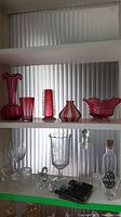 Shelf with cranberry glass vases, candy dish, clear glassware, bottles, and figurines