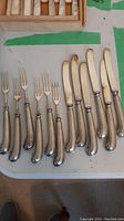 Six appetizer forks and six appetizer knives arranged on tabletop