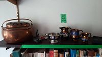 Full view of copper pot, three small pitchers, candle holder on black shelf