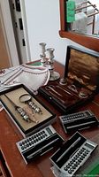 Photo showing manicure set in wooden box with satin interior, two ceramic candle holders with floral design, three pocket calculators and pen, and magnifying glass with letter opener in box.