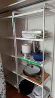 Front view of one metal storage shelf showing five perforated shelves with miscellaneous household items (not included).