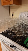 Wide view of assorted clear stemware on stove, showing multiple types of drinking glasses with stems and bases.