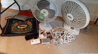 Full view of the lot: two table fans, two aprons, batteries, Samsung flip phone with case, and four white extension cords grouped in a pile.