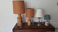 Four table lamps on a dark wood surface against a white wall, showing all four lamps clearly with varying shade colors and base materials.