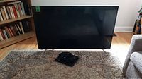 Full front view of the TCL Roku 49-inch TV with Sony DVD player in front on a patterned rug.