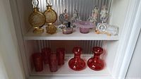 Four cranberry glass tumblers and two cranberry glass vases in deep red glass on bottom shelf