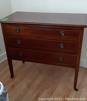 Front view of vintage three drawer wooden dresser with metal ring handles and inlaid drawer edges.