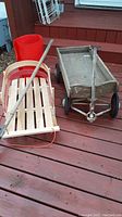 Lot showing all four main items: vintage wooden wagon, children's sled, plastic slider, and hockey stick on wooden deck.