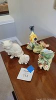 Photo of all four figurines on wooden table showing the cats and colorful goldfinch birds along with the vase with hummingbird and flowers.