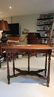 Full front view of antique wooden plant table with four legs and central post showing overall design and condition including water damage on top.