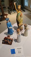 Five assorted figurines shown on table, including tall pregnant daughter figure, graduate girl, teddy bear, and two angels.