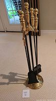 Full view of the fireplace tool set on carpeted floor near a door, showing all four tools with brass handles and black iron shafts on the brass stand.